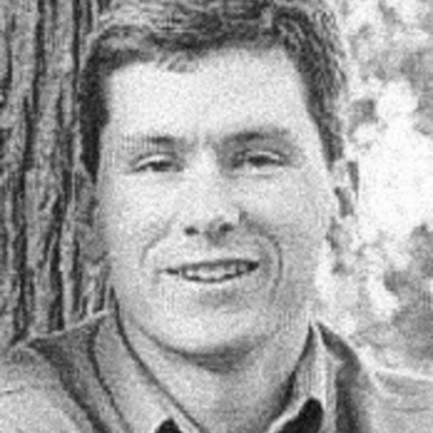 A black and white headshot of Johnny Span, smiling at the camera, in front of a tree.