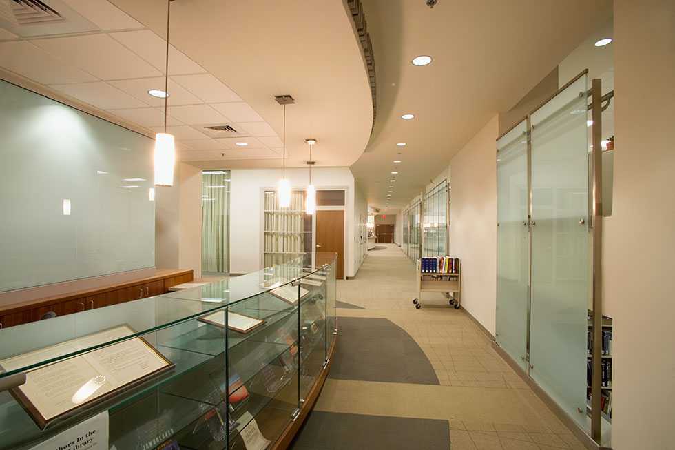 A well-lit hallway with rooms on the right and documents encased in glass display cases on the left.