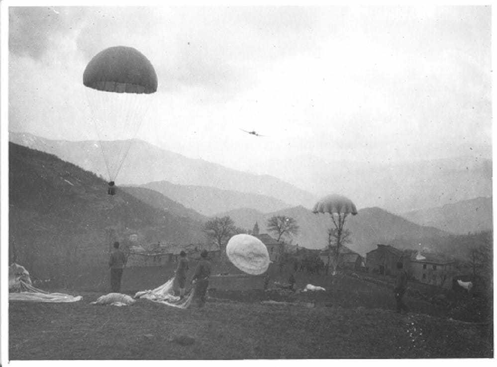 A black and white photograph of OSS officers landing by parachute on to a hill.