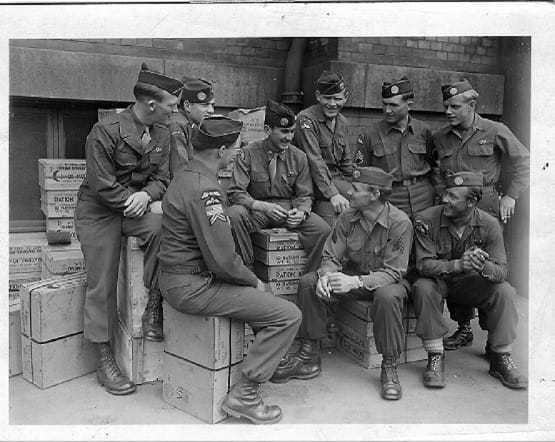 Nine OSS soldiers in uniform engaging in conversation.