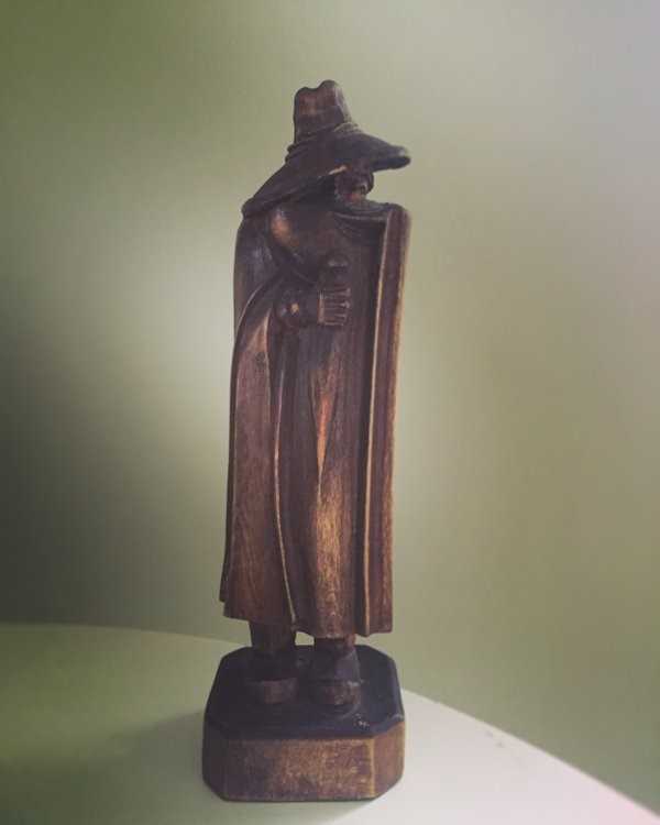 A small wooden carving of a figure in long cloak and large hat drooping down to cover its face.