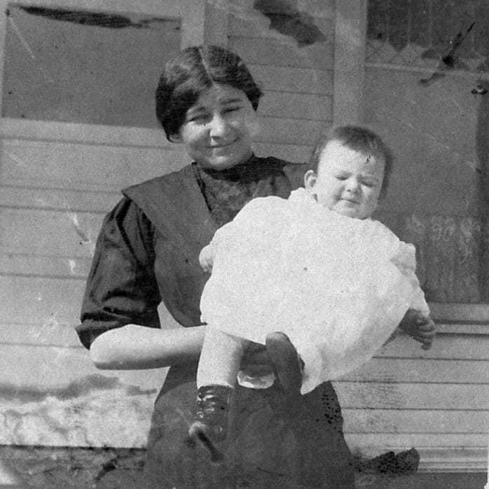 A black and white photograph of Elizabeth as a young infant in white garbs being held by her Sioux nanny.