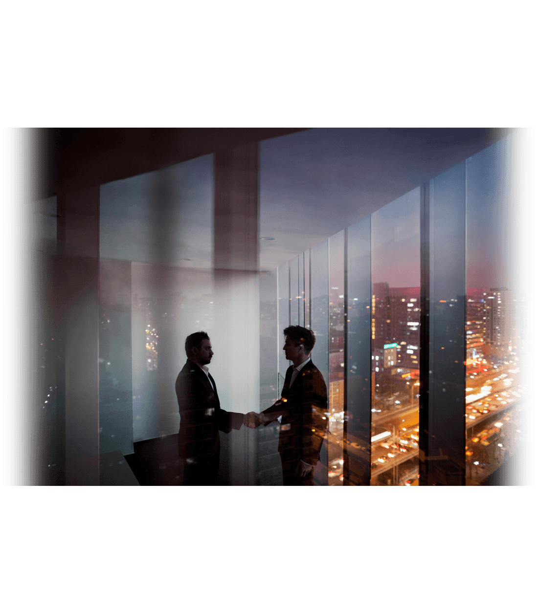 two people shaking hands in front of floor to ceiling windows with city lights behind them