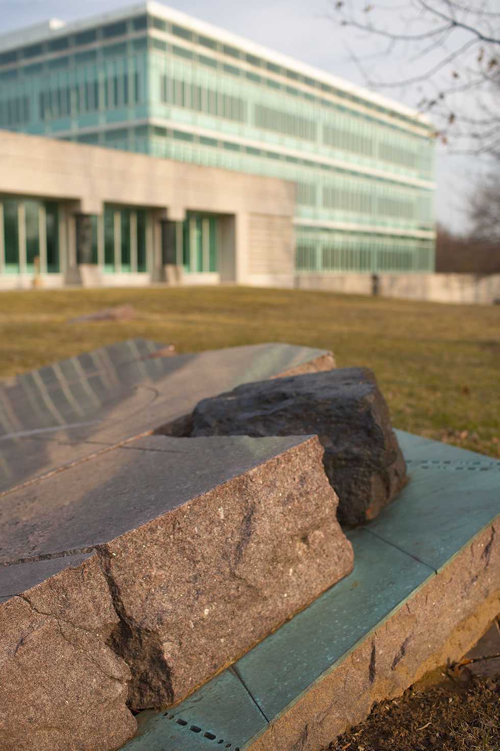 A dark boulder wedged in a divot on a glossed over plaque raised from the ground.