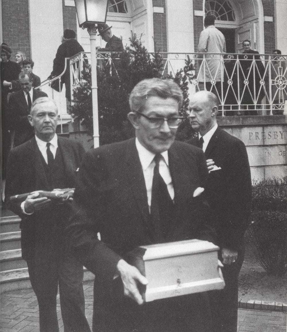 James Angleton holding a box of ashes with two officials standing behind him.