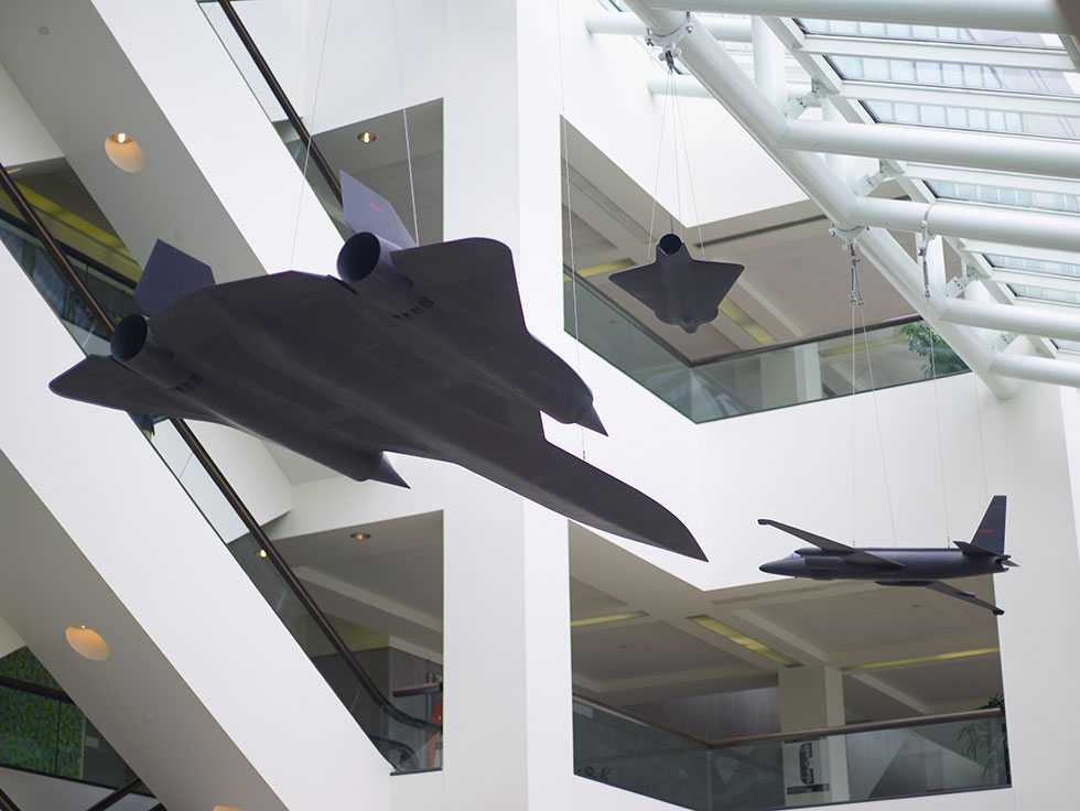 A glass enclosed atrium with three different models of drone replicas suspended from the ceiling.