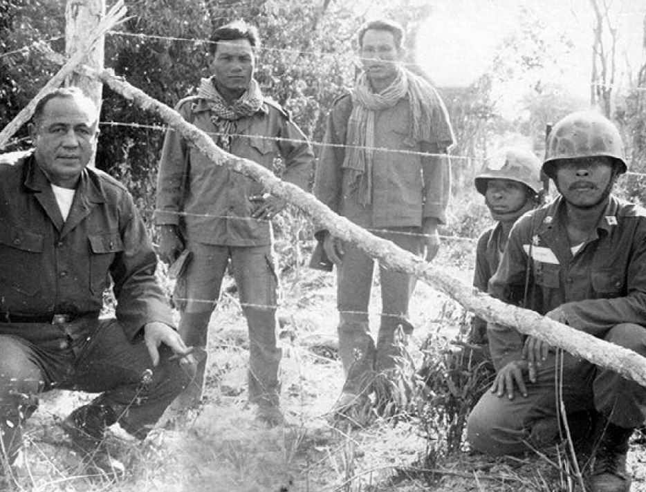 black and white photo of several men kneeling near a fence with two men standing behind the fence.