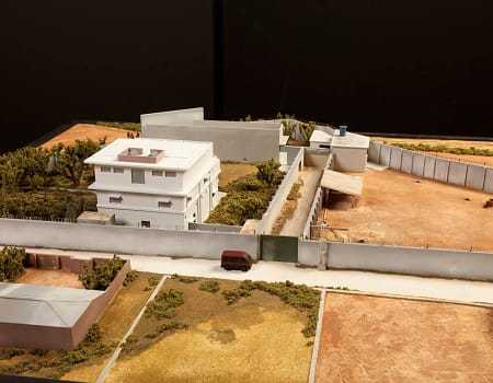 A wide view of the model, with a gate blocking the entrance to the compound from the small road outside.
