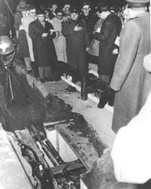A collection of Soviet officials standing next to a hole in the ground exposing an underground tunnel.