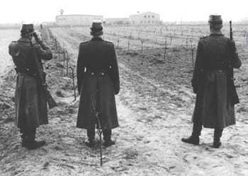 Three East German Police overlooking a field on the compound.