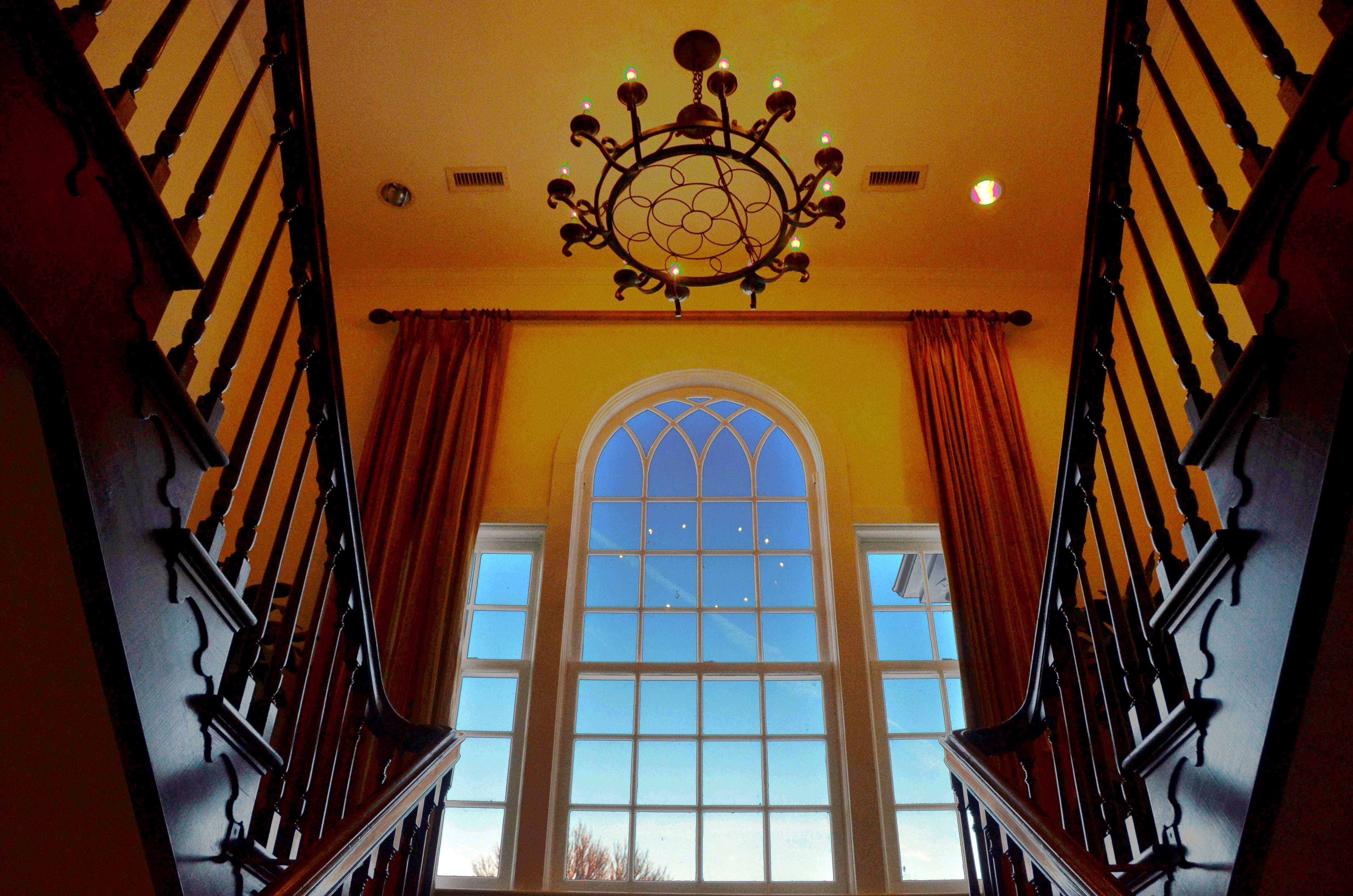 An upward looking shot of a large window and the chandelier at the entrance of the manor.
