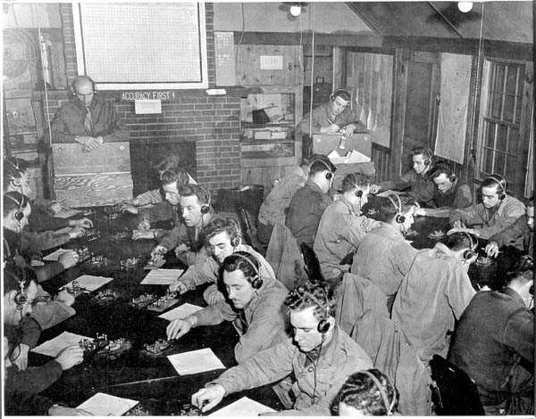 black and white image of young men sitting across from one another at tables, wearing headphones, decoding messages from WWII.