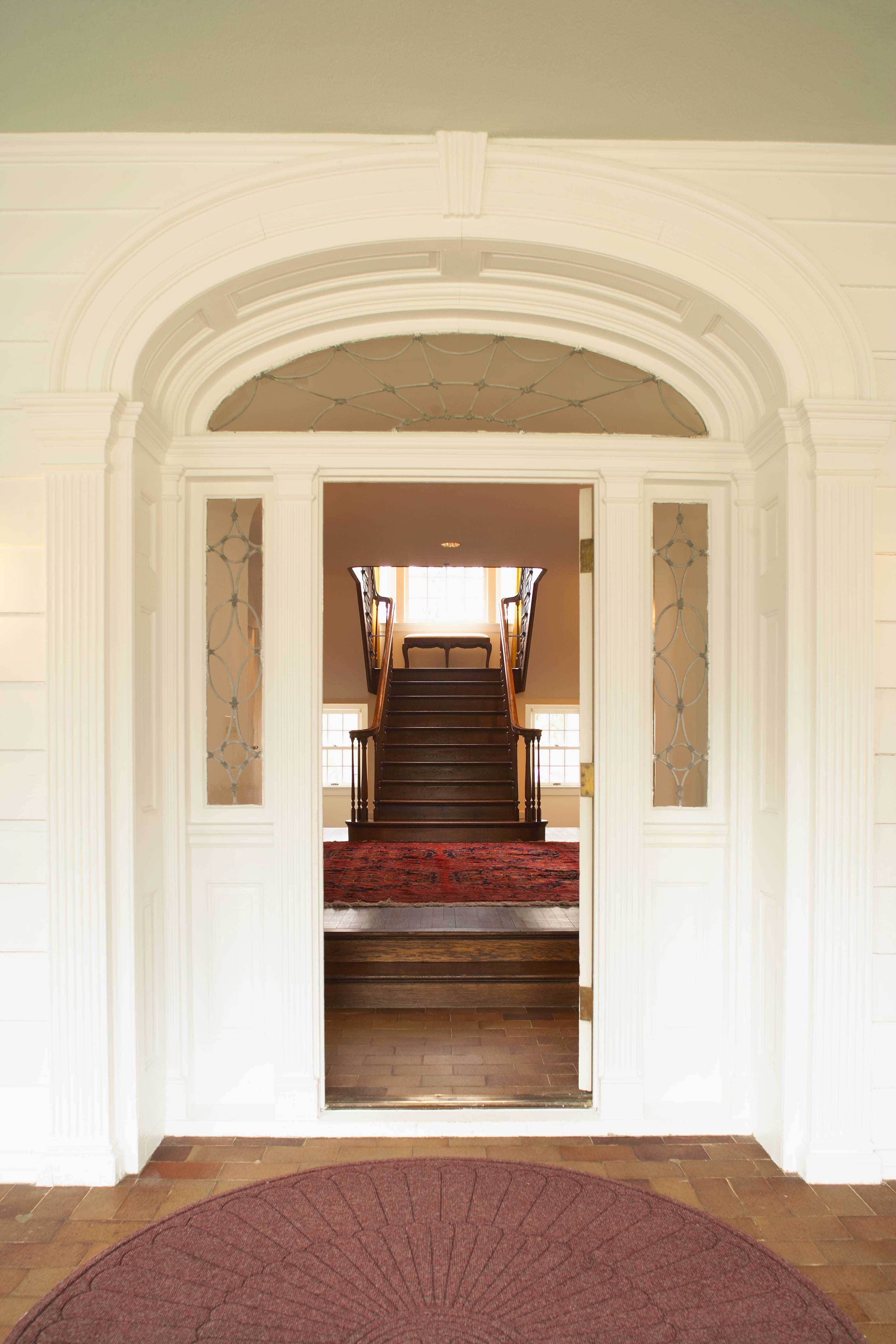 A crisp, white front entrance of the manor with the door opened and a view of the large, wooden staircase.