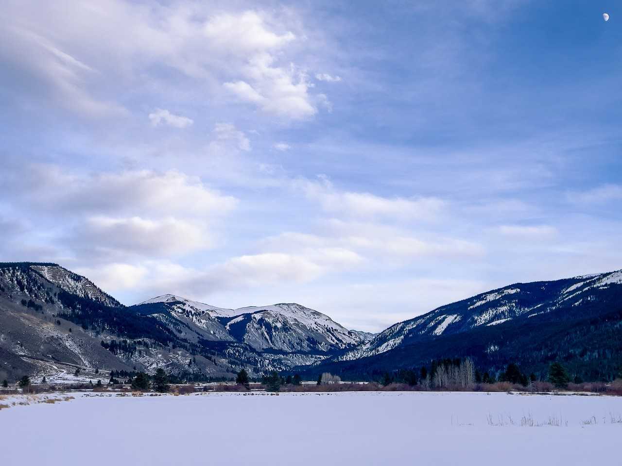 A flat open snowy plain surrounded by high mountains covered in snow.