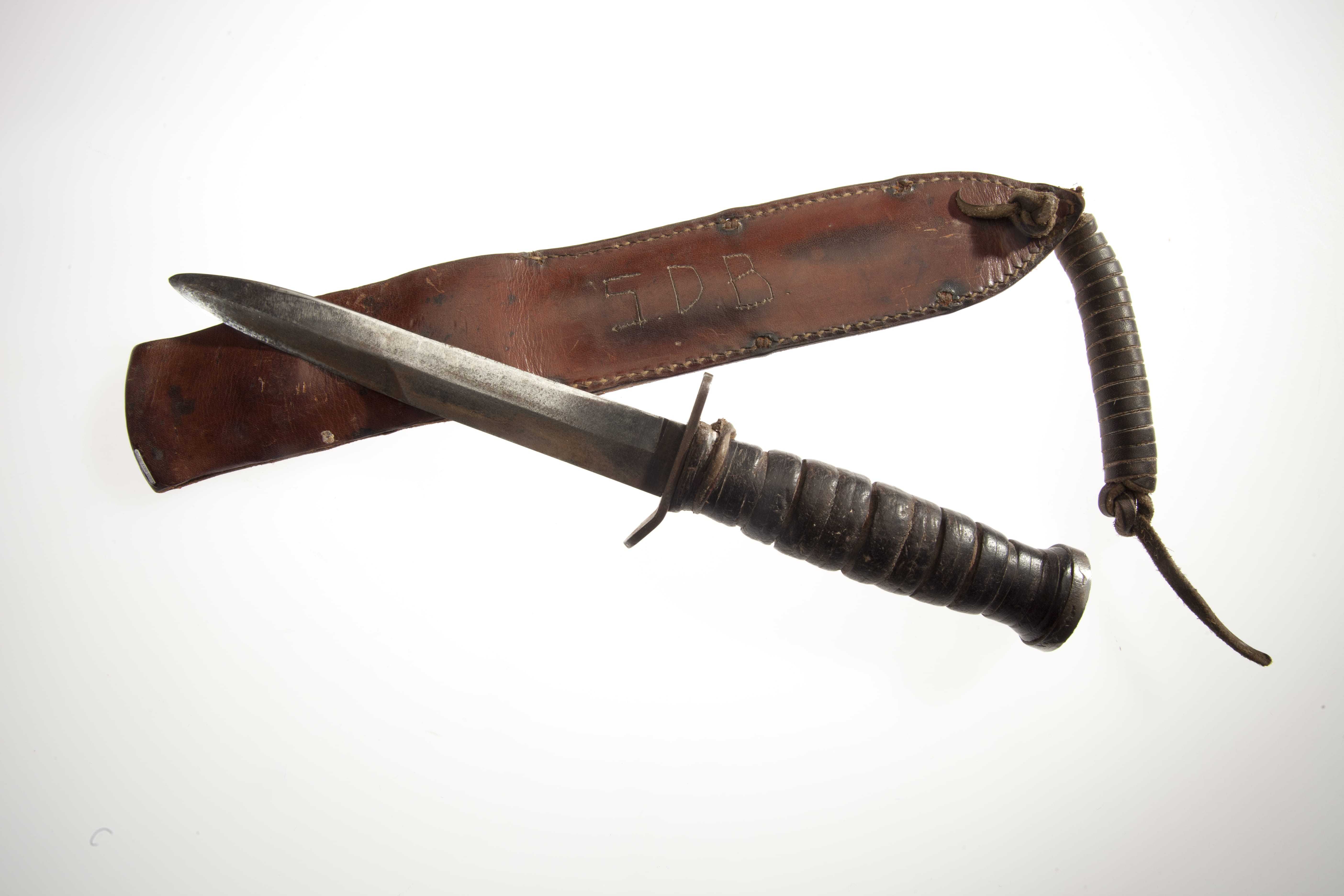 A flat, rounded knife with a wooden handle next to its leather sheath.