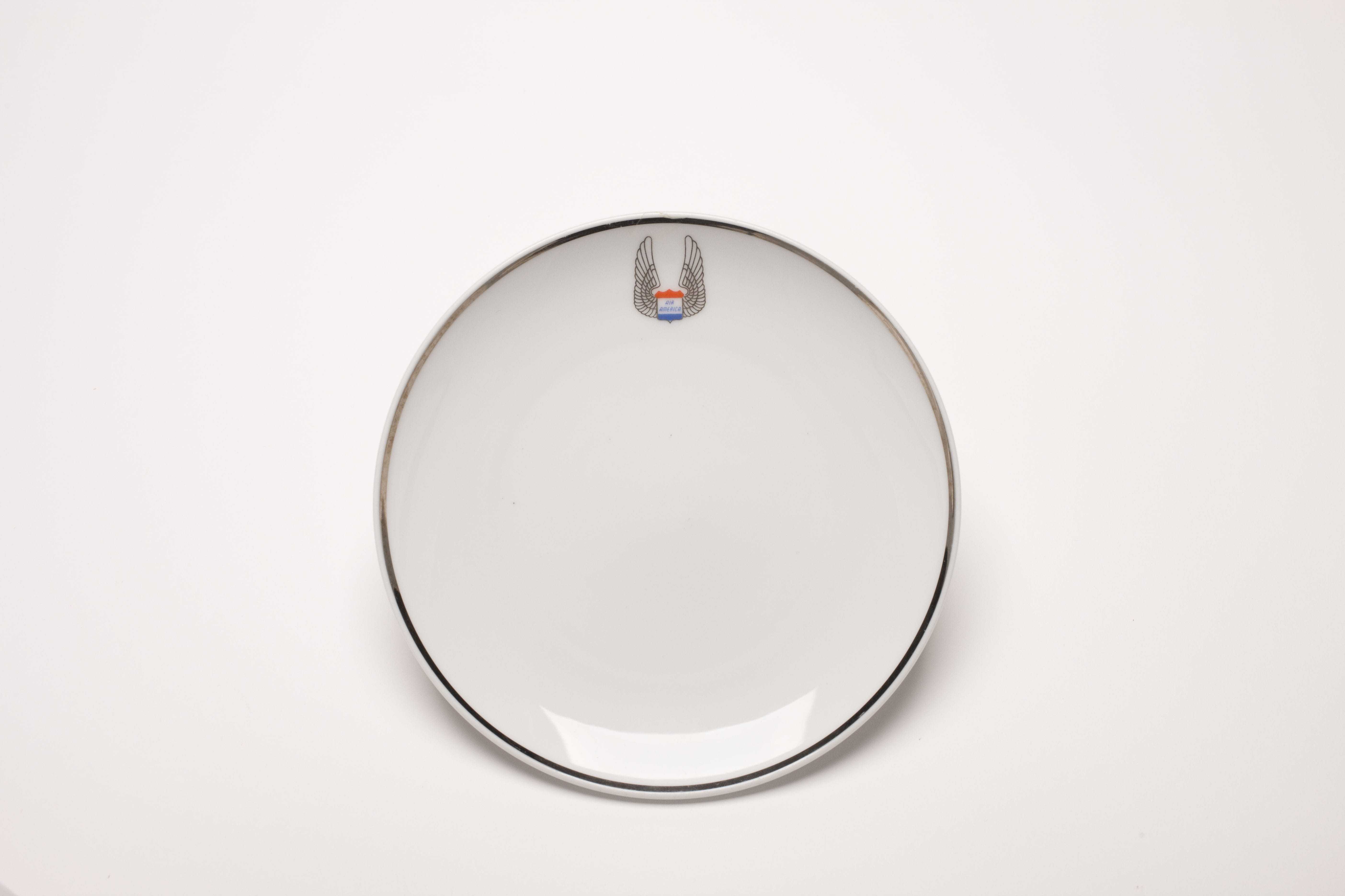 A white dinner plate with a gold rim and the Air America logo at the top