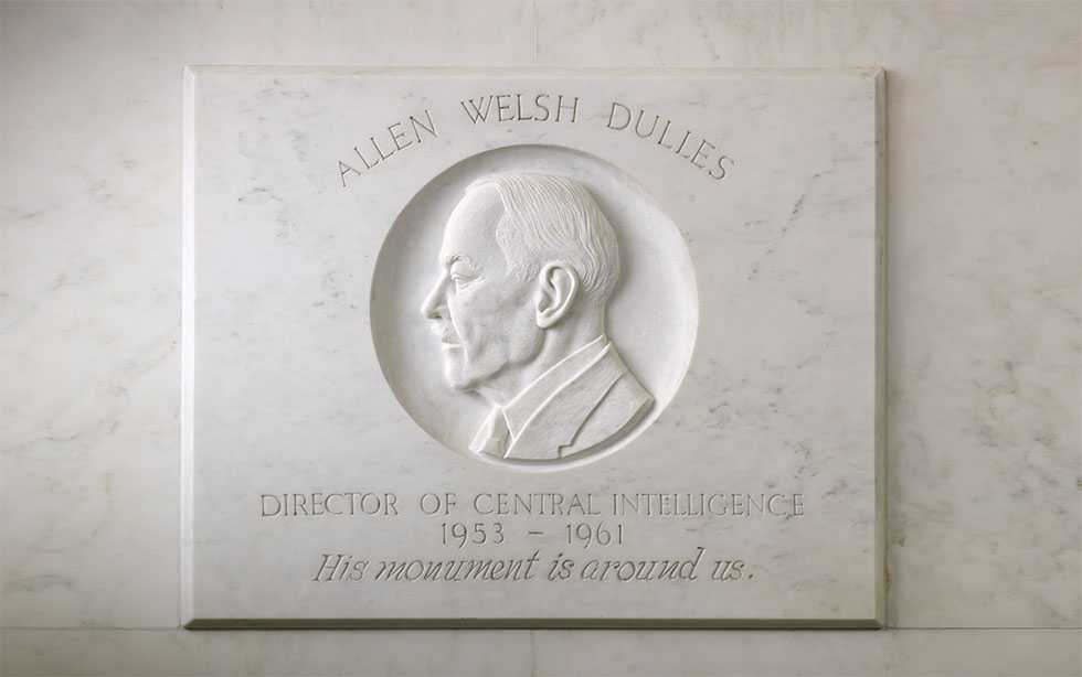 A white, marble bas-relief of a former CIA officer marked by his name, title, birth year and death year.