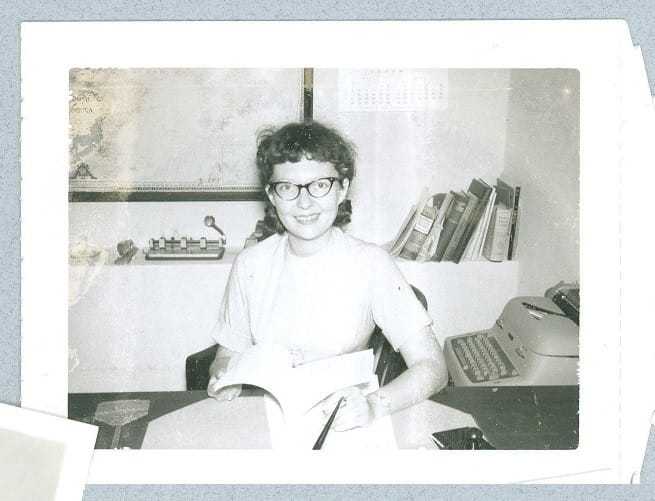 Jeanne Vertefeuille sitting at a desk holding a book open.