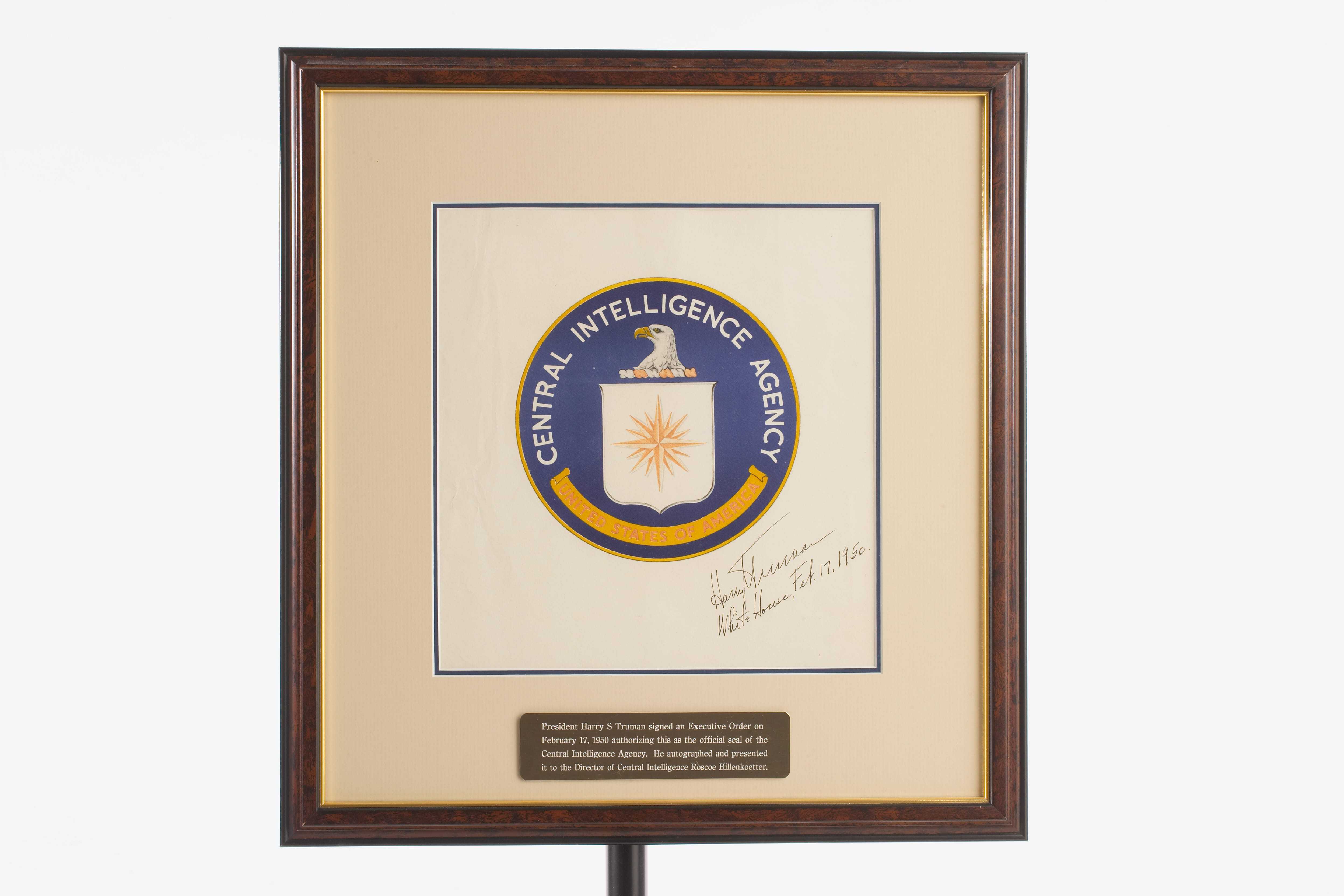 A framed CIA seal signed by Harry Truman and a plaque describing the approval of the seal