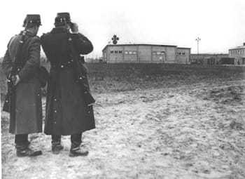 Two East German police looking at a warehouse building on the compound.