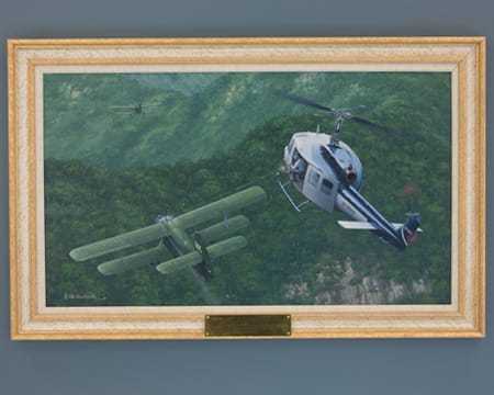 A painting of an Air America helicopter shooting at a North Vietnamese plane