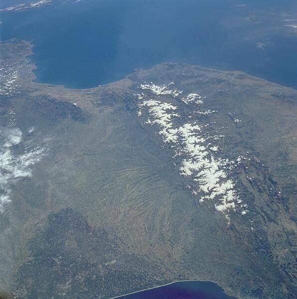 View of the Pyrenees Mountains between France and Spain taken April 1985. The snow-covered mountains, which form a formidable physical barrier between France to the north (left) and Spain to the south (right), are the main focus of this low-oblique, southeast-looking photograph. Scarcely interrupted by accessible passes and pierced in only two places by railroad tunnels, the Pyrenees are an ideal natural boundary between the Iberian Peninsula and the rest of Europe. The northern flank of the Pyrenees is characterized by a series of large alluvial deposits that fan out across southwestern France. The darker, roughly triangular area in southwest France is part of the forested Aquitaine Basin. The southern flank of the Pyrenees (Spain) is characterized by aridity and very rugged, mountainous conditions. Human settlement is sparse throughout the Pyrenees. However, because the region is rich in mineral waters, there are dozens of mineral water resorts, and winter sports attract visitors from southwestern France. The very small mountainous country of Andorra (not distinguishable in this photograph) has survived in an inaccessible upper valley of the Pyrenees. Image courtesy of NASA.