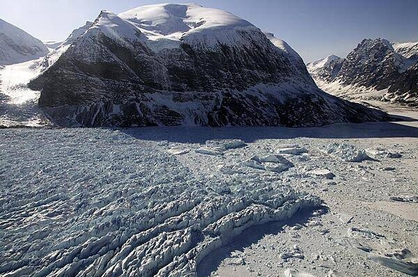 The calving front of Kangerdlugssup Glacier in central west Greenland where icebergs are born. You can see several large ice bergs in the fjord on the right surrounded by the so called m&#xe9;lange, which is a dense mix of bergy bits and sea ice floating in the fjord. The m&#xe9;lange plays a role in how many ice bergs a glacier can produce by stabilizing the calving front. Credit: NASA/Michael Studinger.