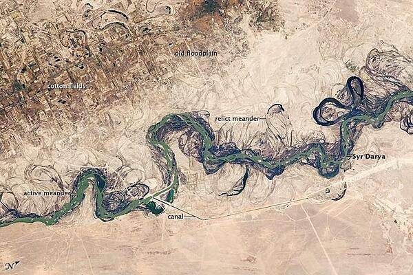 Central Asia&apos;s most important cotton-growing region is concentrated in the floodplain of the Syr Darya. The floodplain is shown here as a tangle of twisting meanders and loops (image center). The darkest areas are brushy vegetation along the present course (filled with blue-green water); wisps of vegetation are also visible along flanking swampy depressions, or sloughs. An older floodplain appears as more diffuse dark vegetation (image upper left), where relict bends are overlain by a rectangular pattern of cotton fields. The straight channel of a new diversion canal can be seen along the east bank of the river. Half the river flow is controlled from reservoirs, and half from direct water take-off from canals. In contrast to the intensive agricultural use of water shown here, water control in the mountain valleys upstream is oriented more toward power generation.
The river flows for 2,200 km (1,370 mi), from the Tien Shan Mountains west and northwest to the Aral Sea. Control of the river is vested in the Syr Darya Basin Water Organization, run by nations with territory in the watershed. Some of the organization&apos;s main efforts include accurate gauging of water use and repair of canals to reduce widespread water leakage. Photo courtesy of NASA.