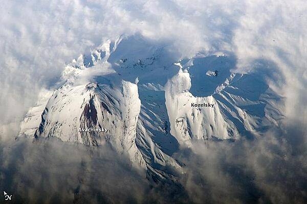 Russia&apos;s eastern Kamchatka Peninsula, which extends far into the Pacific Ocean, includes more than 150 volcanoes. While most are not actively erupting, many are considered dangerous due to their eruptive history and proximity to population centers and air travel corridors. This astronaut photo highlights the summit crater and snow-covered slopes of Avachinshy stratovolcano (2,741 m; 8,993 ft) as it pokes above a surrounding cloud deck. The volcano has an extensive historic and geological record of eruptions, the latest activity ocurring in 2008. To the southeast (image right), the large breached crater of Kozelsky volcano also appears above the clouds. Kozelsky is a parasitic cone, formed by the eruption of material from vents along the flank of Avachinsky. Photo courtesy of NASA.