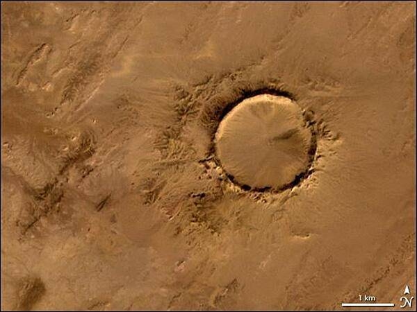 Deep in the Sahara lies a crater, a nearly a perfect circle that is 1.9 km (1.2 mi) wide, and sports a rim 100 m (330 ft) high. The Tenoumer crater sits in a vast plain of rocks so ancient they were deposited hundreds of millions of years before the first dinosaurs walked the Earth. Close examination of the structure has revealed that the crater&apos;s hardened &quot;lava&quot; was actually rock that had melted from a meteorite impact.

On this satellite image the crater&amp;apos;s outline is unmistakable, yet it does not necessarily look like a crater; the light and shadows make it look more as if someone pressed a giant cookie cutter into the rock. In this image, the sunlight shines from the southeast (lower right), and the bright arc along the northwestern part of the crater is where the crater walls slope up to the rim. Around the perimeter, the relatively steep walls cast dark shadows. Although it resides in ancient rock, Tenoumer is geologically young, ranging in age between roughly 10,000 and 30,000 years old. Photo courtesy of NASA.