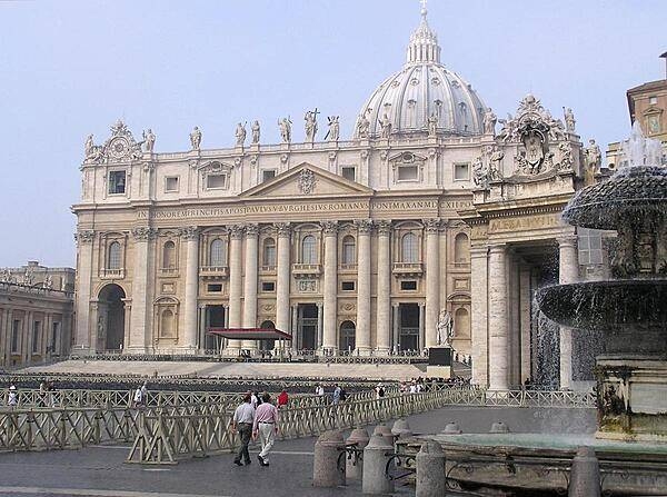The facade of St. Peter&apos;s Basilica as viewed from next to one of the two matching Bernini fountains that grace St. Peter&apos;s Square (Piazza) in front of the church. The attic or upper story displays statues of Christ, his apostles, and St. John the Baptist. Constructed over a period of 80 years and consecrated in 1626, the basilica is the largest Christian church in the world - capable of holding some 60,000 people.