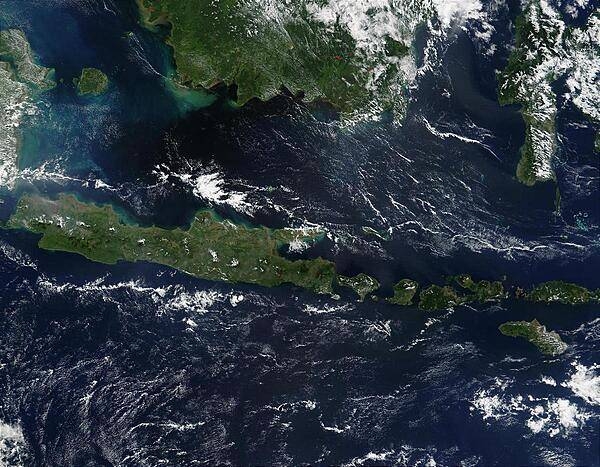 This true-color image of some of the Indonesian islands is from mid-May 2002. Fire season was not fully underway in the region, and skies over the large island of Borneo (top) were partially cloud-covered, but not hazy with air pollution. The horizontally situated island of Java appears to be experiencing some haze at its western end, and a few scattered fires (red dots) are apparent. Image courtesy of NASA.