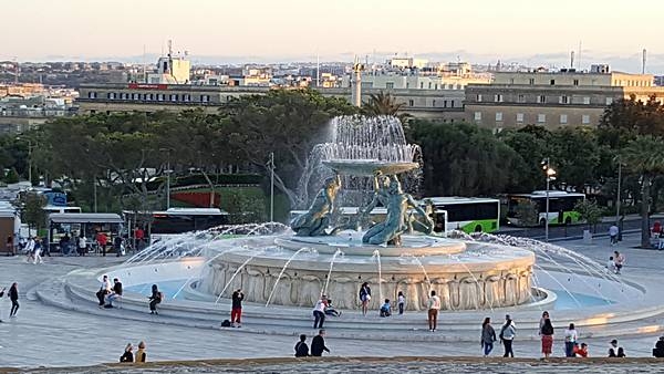 The Fountain of the Three Tritons, designed by Vincent Apap, stands outside of Valetta's main city gate. Fully constructed and completed in 1959, the fountain depicts three bronze half-human, half-mermen, two sitting while the third one kneeling, holding a bronze platter on a seaweed base. They symbolize strength and Malta’s relation to the Mediterranean Sea. In Greek mythology, Triton was Poseidon’s son and messenger of the sea. Over time, Triton(s) came to mean mermen in general.