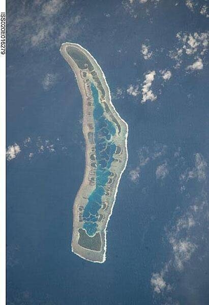 Millennium Island - known as Caroline Island prior to 2000 - is located at the southern end of the Line Islands, which make up the western portion of Kiribati. Uninhabited Millennium Island is formed from a number of smaller islets built on coral reefs. The reefs grew around a now-submerged volcanic peak, leaving a ring of coral around an inner lagoon. The shallow lagoon waters are a lighter blue than the deeper surrounding ocean water; tan linear &quot;fingers&quot; within the lagoon are the tops of corals. The two largest islets are Nake Islet (on the north) and South Islet. Image courtesy of NASA.
