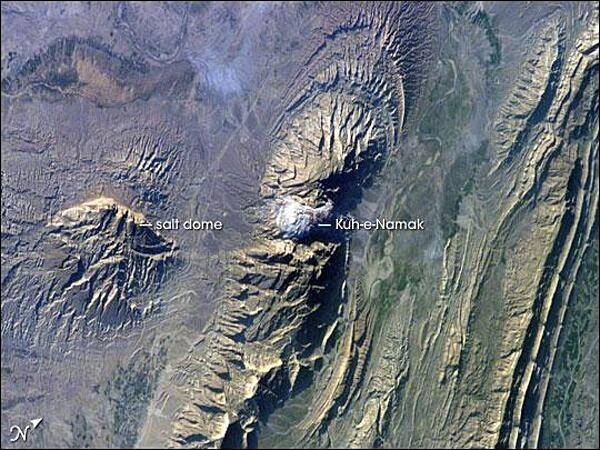 The Zagros Mountains in southwestern Iran present an impressive landscape of long linear ridges and valleys. Formed by collision of the Eurasian and Arabian tectonic plates, the ridges and valleys extend hundreds of kilometers. This astronaut photograph of the southwestern edge of the Zagros mountain belt includes another common feature of the region - a salt dome (Kuh-e-Namak or &quot;mountain of salt&quot; in Farsi). Thick layers of minerals such as halite (table salt) typically accumulate in closed basins during alternating wet and dry climatic conditions. Over geologic time, these layers of salt are buried under younger layers of rock. The pressure from overlying rock layers causes the lower-density salt to flow upwards, bending the overlying rock layers and creating a dome-like structure. Erosion has spectacularly revealed the uplifted tan and brown rock layers surrounding the white Kuh-e-Namak to the northwest and southeast (center of image). Radial drainage patterns indicate another salt dome is located to the southwest (image left center). If the rising plug of salt (called a salt diapir) breaches the surface, it can become a flowing salt glacier. Salt domes are an important target for oil exploration, as the impermeable salt frequently traps petroleum beneath other rock layers. Image courtesy of NASA.