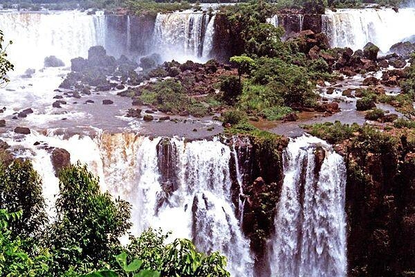 A panoramic view of Iguazu Falls along the Brazil-Argentina border. The falls are shared between Iguazú National Park (Argentina) and Iguaçu National Park (Brazil). The two parks were designated UNESCO World Heritage Sites in 1984 and 1986, respectively. The entire waterfall system consists of some 275 falls that flow over several basaltic layers over an 80 m height and along 2.7 km (1.7 mi) of the Iguazu River. The many cascades producing vast sprays of water to create one of the most spectacular waterfalls in the world. The falls are easily reached from either side of the Argentine–Brazilian border.