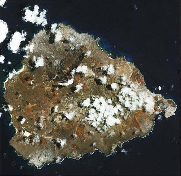 In the southern Atlantic Ocean roughly midway between central South America and central Africa, sits Ascension Island. A small, rocky, volcanic outcrop covered in many places by lava flows and cinder cones of dormant volcanoes, the island sits just west of the Mid-Atlantic Ridge. In this detailed satellite image taken 24 February 2003, marbled-looking lava flows can be seen dominating the northwest coast, with smaller flows visible on the southwest coast below the island's Wideawake Airfield, as well as on the southeast coast. Northeast of the airstrip, a large cinder cone is visible, its dark brown center fading to tan in a series of pale rings. This crater, the island's largest, is called Devil's Riding School. Crisp, white surf breaks along the shores. Image courtesy of NASA.