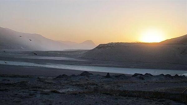 Sunrise at Kangerlussuaq, Greenland, with ravens on the left, and the Watson River and Sugarloaf Hill seen through a haze of windblown glacial silt. Credit: NASA/Jim Yungel.