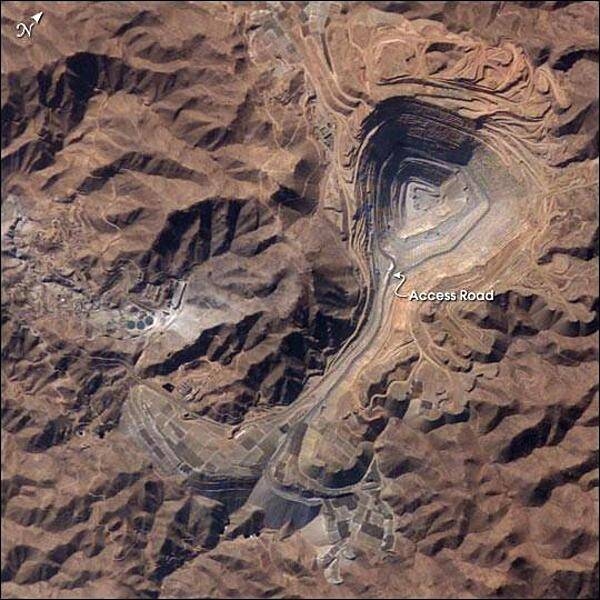 The rugged, mineral-rich Andes support some of the world's biggest mines (gold, silver, copper, and more). This image looks down the bull's-eye of Peru's Toquepala copper mine, a steep sided and stepped open-pit mine. Mid-afternoon sunlight on the arid slopes of the central Andes mountains provides an accent to the mine contours. At the surface, the open pit is 2.5 km (1.5 mi) across, and it descends more than 700 m (2,300 ft) into the earth. A dark line on the wall of the pit is the main access road to the bottom. Spoil dumps of material mined from the pit are arranged in tiers along the northwest lip of the pit. Numerous angular leaching fields appear lower right, and the railroad to the coast is a line that exits the image center left. The railroad was built to export Toquepala's copper and connects the coastal port of Ilo, 95 km (60 mi) to the southwest. Photo courtesy of NASA.