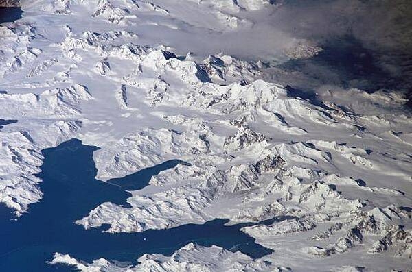 An oblique view of the rugged and isolated landscape on the northern shore of South Georgia Island. The high mountains protect the north and eastern coast of the island from the prevailing gales coming from Antarctica and the west. The steep topography also makes deep embayments along the coast that provide habitat for wildlife and anchorages for whaling ships. The island supports major rookeries of penguins and albatrosses, and large seal populations. This view centers on Mt. Paget and Cumberland Bay. Image courtesy of NASA.