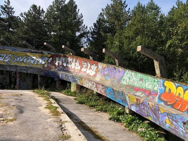 Trebevic Mountain, located outside of Sarajevo, was the site of many 1984 Winter Olympics events. During the 1,425-day Siege of Sarajevo, Trebevic was heavily mined, and its elevation provided an ideal position for snipers and artillery units attacking Sarajevo. Following lengthy restoration work, the mountain was declared a national park and reopened to the public in 2017. In 2014 the International Luge Federation, the ZOI’84 Olympic Legacy Foundation, the National Bobsleigh Federation, and volunteers began work on the restoring the damaged track and today it is used by bicyclists, skateboarders, and for summer luge training. The graffiti-covered track is also a cultural landmark and beloved by admirers of street art the world-over.