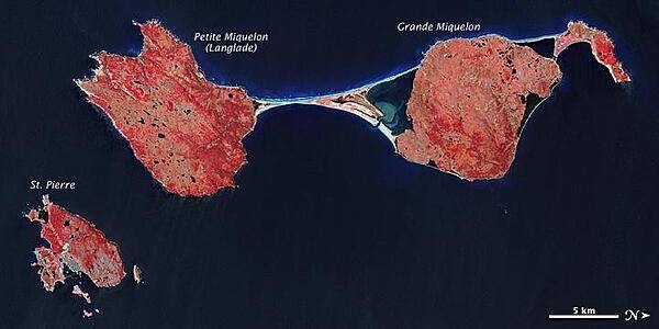 The last remnant of France&apos;s once-vast holdings in North America, this island archipelago off the coast of Newfoundland bears the scars of a complicated geologic history. Saint Pierre and Miquelon cover just 242 sq km (93 sq mi), and the three biggest islands lend the entire archipelago its name.
In this false-color satellite image, vegetation appears in varying shades of pink and red, bare land is beige, urbanized areas are blue-gray, and water appears in shades of blue and blue-green.
Saint Pierre is the smallest of the archipelago&apos;s major islands, a mostly northeast-southwest running landmass with several smaller islands and islets scattered around it. In the west (top of the image), Miquelon consists of three main sections: an arc-shaped body in the north (top right), Grande Miquelon immediately southeast of that, and Langlade (or Petite Miquelon) Island in the south. Grande Miquelon and Langlade are connected by a tombolo, a ridge of beach material (typically sand), built by wave action, that connects an island to the mainland. This tombolo formed in the eighteenth century.
The terrain of the archipelago consists of mostly barren rock. Deforestation has claimed much of the vegetation, although woodland still covers 20 percent of the surface. Scrub vegetation and peatland are extensive. Cold, wet, foggy weather predominates, with windy springs and autumns. 
The islands, particularly Langlade, bear a scoured appearance, and this is no coincidence. During the Pleistocene Ice Age, glacial ice scraped the island. Today, wind and waves continue to erode these landmasses. For several months a year, winds regularly exceed 60 km (35 mi) per hour, and frequent storms pound the coastlines with high waves. Anecdotal evidence from local fishermen suggests that recent mild winters and less extensive sea ice might have allowed more erosion by ocean waves. Photo courtesy of NASA.