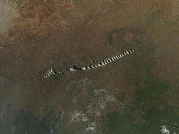 The image shows wave clouds rippling over a fire-speckled Central African Republic landscape. Wave clouds typically form when a mountain, island, or even another mass of air forces an air mass to rise, then fall again, in a wave pattern. The air cools as it rises, and if there is moisture in the air, the water condenses into clouds at the top of the wave. As the air begins to sink, the air warms and the cloud dissipates. The result is a line of clouds marking the crests of the wave separated by clear areas in the troughs of the wave. Each red “hotspot” marks an area of actively burning fires deliberately set to manage the land. Image courtesy of NASA/ Jeff Schmaltz.