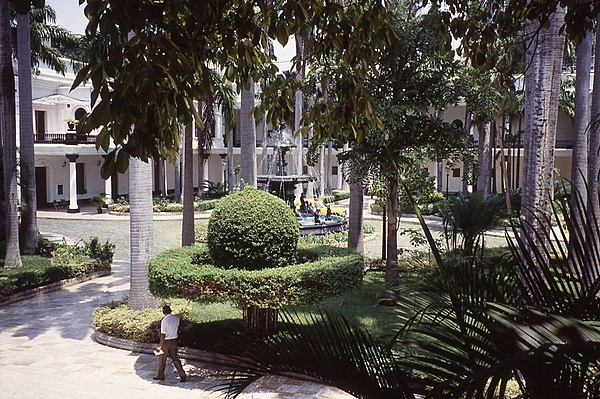 The large courtyard of the Federal Legislative Palace in Caracas is beautifully landscaped with large trees, shrubs, and a fountain.