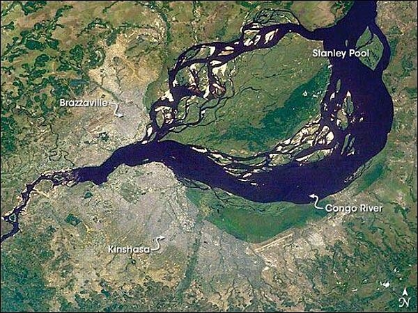 This astronaut image shows two capital cities (brownish-gray areas) on opposite banks of the Congo River. The smaller city on the north side of the river is Brazzaville, while the larger, Kinshasa, is on the south side. The cities lie at the downstream end of an almost circular widening in the river known as Stanley Pool. The international boundary follows the south shore of the pool (roughly 30 km in diameter). The Republic of the Congo, originally a French colony, is sometimes called Congo-Brazzaville - as opposed to the Democratic Republic of the Congo (known from 1971 to 1999 as Zaire) which is often called Congo-Kinshasa, originally a Belgian colony. Brazzaville's population is less than a tenth of Kinshasa's. There is no bridge between the cities so that water craft of many kinds ply between them. It is not uncommon to see dugout canoes being paddled between the cities. Photo courtesy of NASA.