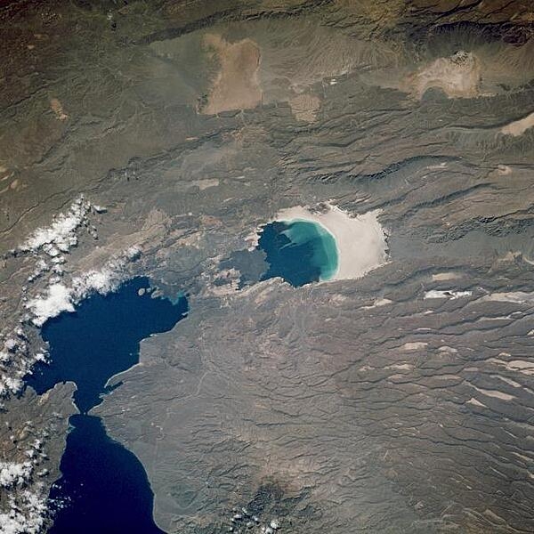 This near-vertical photograph shows Lac Assal (Lake Assal) in Djibouti, the third lowest surface in the world (excluding the ocean basins) and the lowest point in Africa at 155 m (510 ft) below sea level. Lake Assal sits in a rift valley, a depression where the earth&apos;s crust has split and adjacent areas have moved with respect to one another. The lake is located in the Danakil Desert near the western end of the Gulf of Aden. Because Lac Assal has no outlet, it is ten times saltier than the ocean and is the most saline body of water in the world. The evaporation rate of Lake Assal is very high because summer temperatures sometimes reach 52&#xb0;C (125&#xb0;F), and are accompanied by strong dry winds. The surrounding plain (visible on the image to the right of the lake), once the lake floor, is a glistening expanse of salt. The region surrounding the lake is mostly a stony desert with isolated plateaus and highlands. Lava flows from an ancient volcano are visible just to the left near the shore of the lake. Image courtesy of NASA.