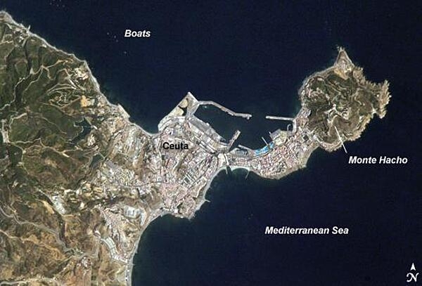 The small Spanish enclave of Ceuta occupies a narrow isthmus of land on the African side of the Strait of Gibraltar; the rest of the surrounding territory is Morocco. Densely populated Ceuta occupies the center of the image, its pink and white residential and industrial rooftops occasionally broken by patches of green - city parks and athletic fields. North of the city, seawalls enclose a small bay and harbor. On the beach, bright blue patches are large water parks. The Spanish fort at Monte Hacho on the eastern isthmus tip commands a clear view of the Strait. Image credit: NASA.