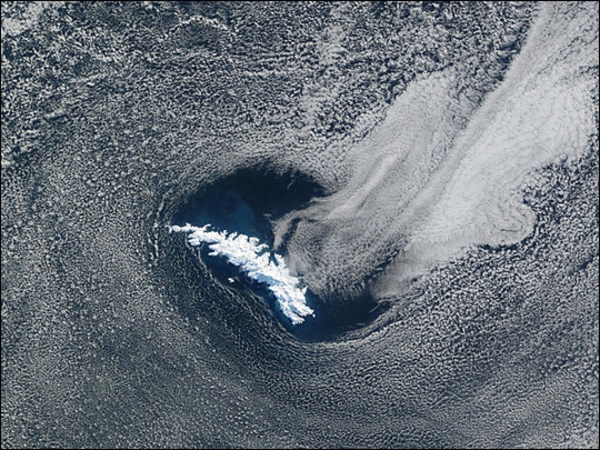 This satellite view shows a break in the cloud cover that frames South Georgia Island in the South Atlantic Ocean. Phytoplankton appears to be in bloom around the island giving the waters a lighter, more turquoise hue. Image courtesy of NASA.
