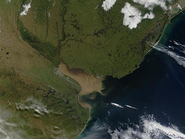 The Rio Parana in Argentina (running north-south through image center) appears brown from its sediment; it eventually drains into the Delta del Parana and the Rio de la Plata estuary. Where the Rio de la Plata empties into the Atlantic, the brown, sediment-filled river water mixes with clearer ocean water and creates swirls and cloudy formations. Visible in this image (in gray) is Buenos Aires, the capital city of Argentina, located where the Rio Parana meets the Rio de la Plata. Montevideo, Uruguay&apos;s capital, is located on the opposite side of the Rio de la Plata. Photo courtesy of NASA.