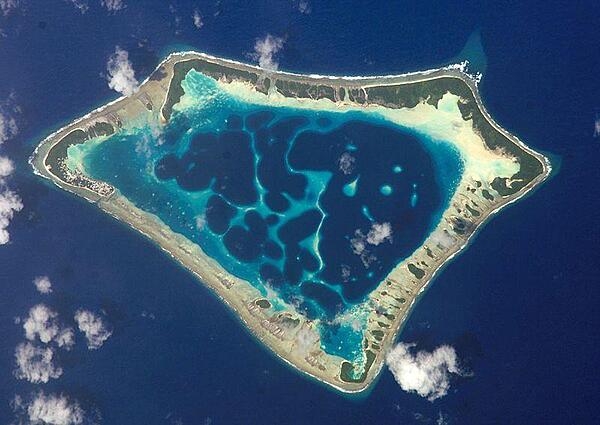 At roughly 8 km (5 mi) wide, Atafu Atoll is the smallest of three atolls comprising Tokelau. Land area is only about 2.5 sq km and the lagoon&apos;s area is about 15 sq km. The primary settlement on Atafu is a village located at the northwestern corner of the atoll - indicated by an area of light gray dots in the left part of this photograph. The typical ring shape of the atoll is the result of coral reefs building up around a former volcanic island. Over geologic time, the central volcano subsided beneath the water surface, leaving the fringing reefs and a central lagoon that contains submerged coral reefs. Image courtesy of NASA.